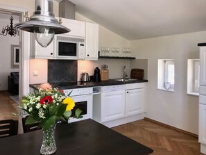 Een moderne keuken met witte kastjes, een magnetron, een spoelbak en een eethoek met een bloemenvaas.