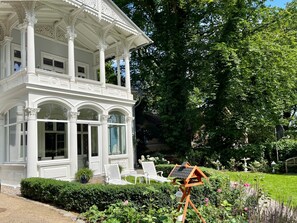 A white gazebo with ornate columns and a covered porch, surrounded by a well-maintained garden with hedges and flowering plants. - a. First floor - Floor - Villa Achterkerke (Heringsdorf)