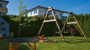 Een achtertuin met een houten schommelset, een picknicktafel en een huis op de achtergrond.