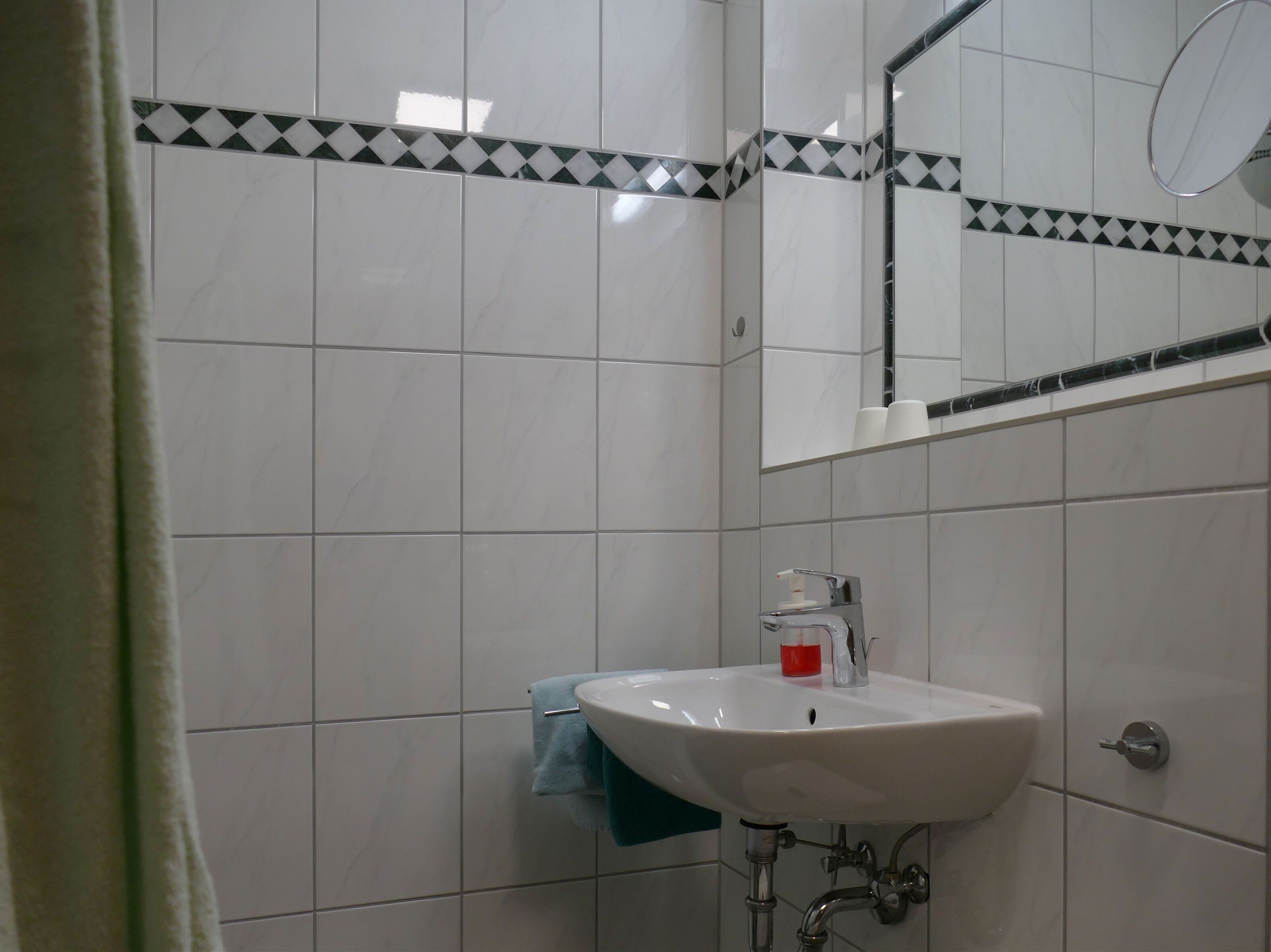 A bathroom with white tiles, a sink, a mirror, and a towel rack.