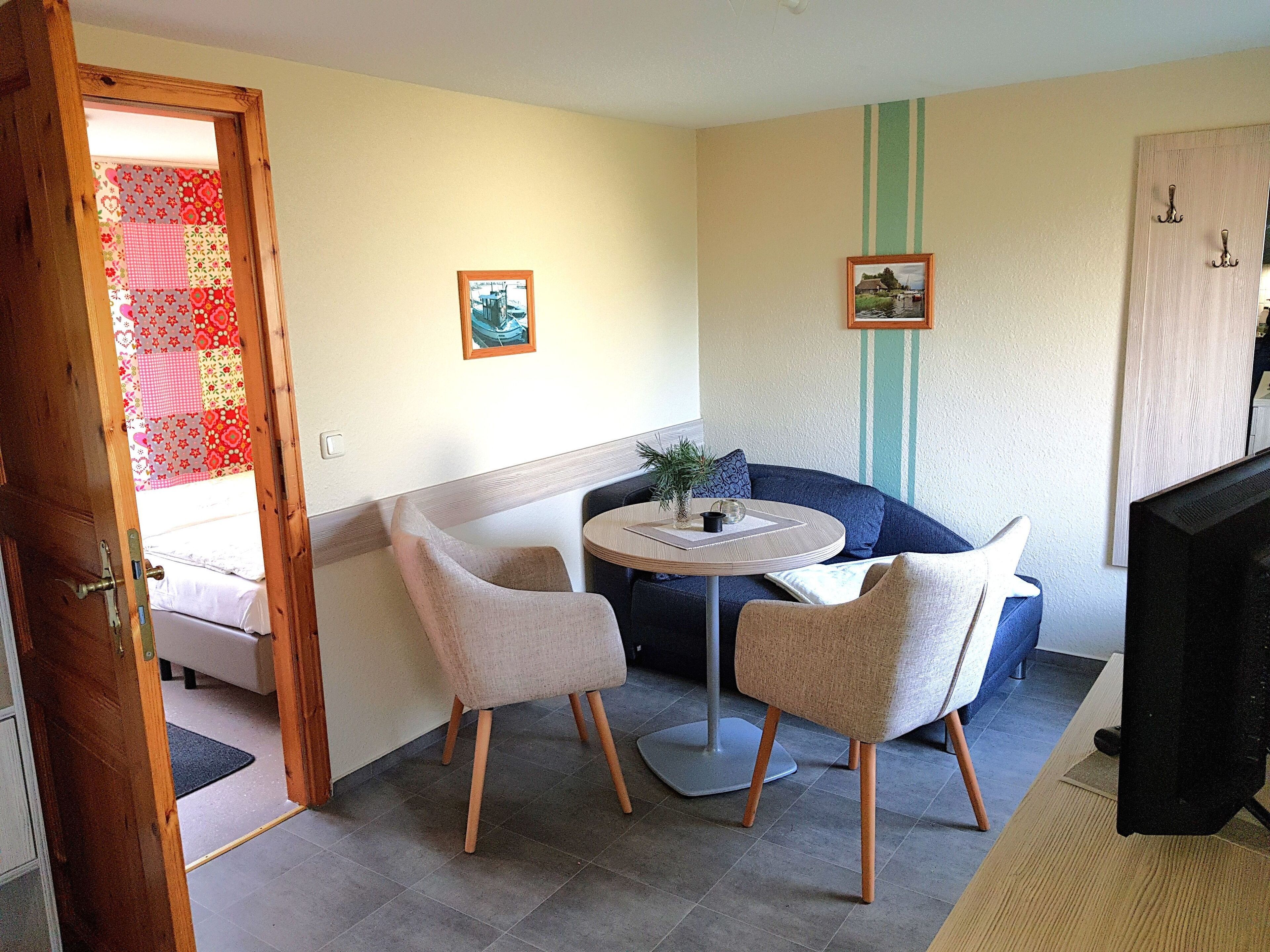 A small, cozy room with a round table, two chairs, a sofa, and a television.