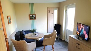A cozy living room with a round table, two chairs, a sofa, a television, and a cabinet. - Apartment 6 - Ferienhof Letzter Heller (Karlshagen)