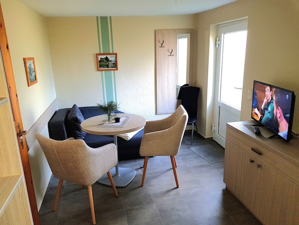 A cozy living room with a round table, two chairs, a sofa, a television, and a cabinet.