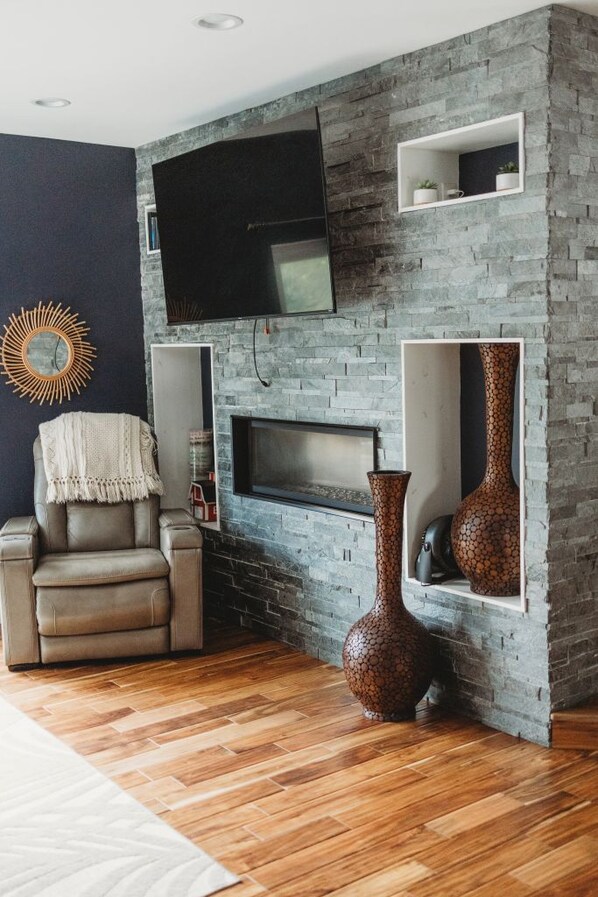 A living room with a stone wall, a flat-screen TV, a fireplace, and a large vase.