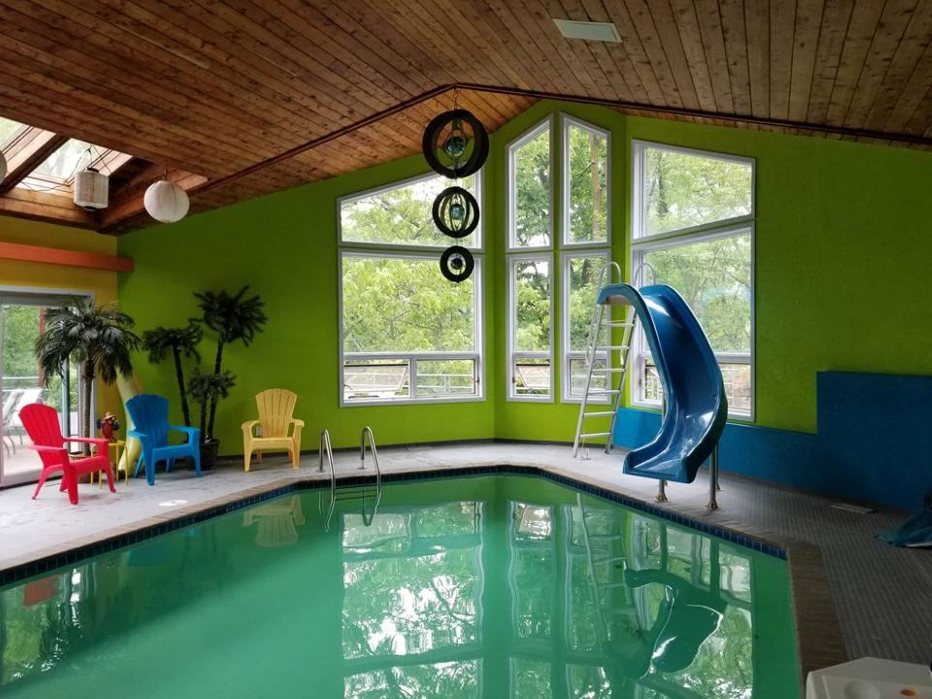 Una piscina al coperto con uno scivolo, ampie finestre e sedie colorate.