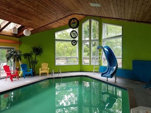 An indoor swimming pool with a slide, large windows, and colorful chairs. - Ultimate Wisconsin Indoor Resort Getaway: 8000 sq feet, indoor pool, & game room (Ripon)