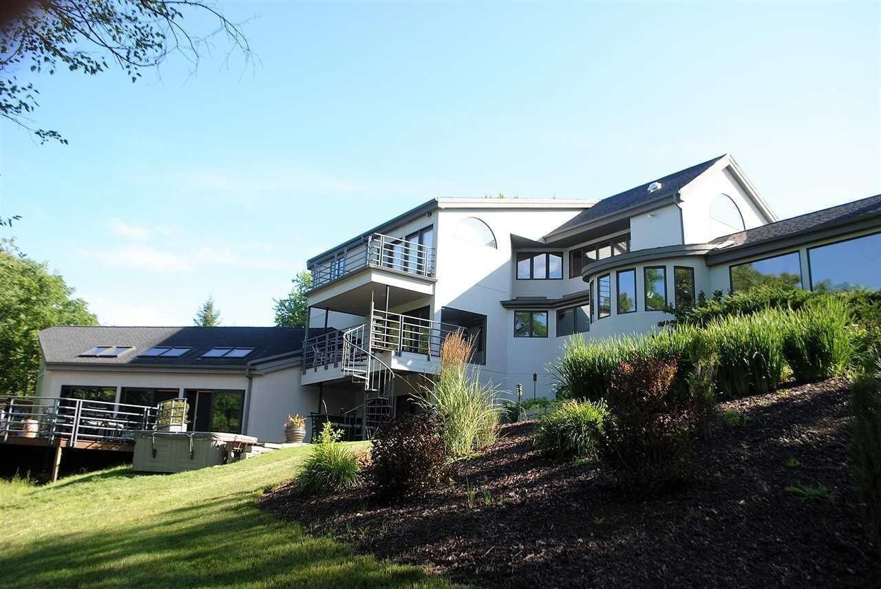 A modern two-story house with a balcony, a covered patio, and a landscaped garden.