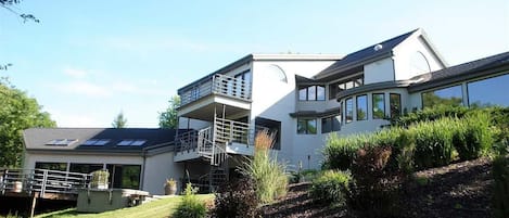 A modern two-story house with a balcony, a covered patio, and a landscaped garden.