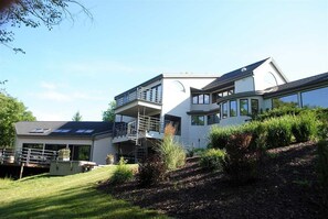Een modern huis met twee verdiepingen, een balkon, een overdekte patio en een aangelegde tuin.