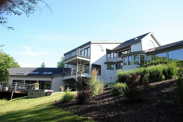 A modern two-story house with a balcony, a covered patio, and a landscaped garden. - Ultimate Wisconsin Indoor Resort Getaway: 8000 sq feet, indoor pool, & game room (Ripon)