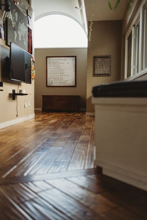 Une pièce avec un plancher en bois, un téléviseur fixé au mur et une liste encadrée des règles de la maison.