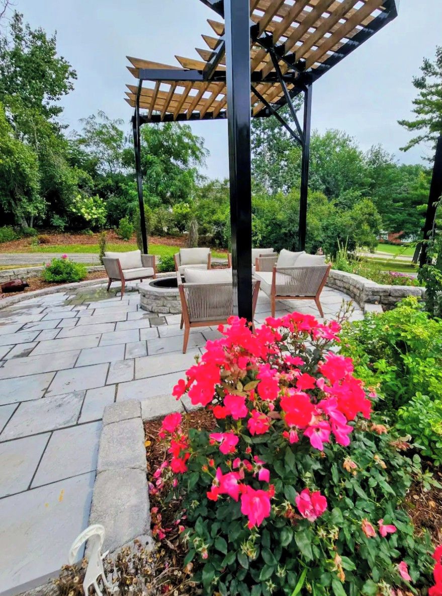 An outdoor patio area with stone flooring, a wooden pergola, and a seating arrangement.