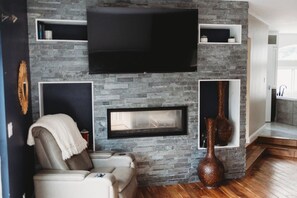 Un salon avec un mur en pierre, un téléviseur à écran plat, une cheminée et un canapé.