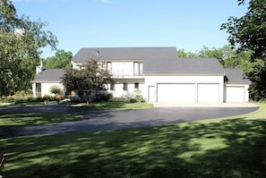 Een twee verdiepingen tellend huis met garage, omringd door een verzorgd gazon en bomen.
