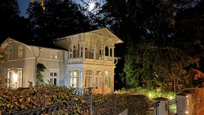 Un grand bâtiment imposant, orné de nombreuses fenêtres et doté d’un balcon, entouré d’une clôture et d’arbres.