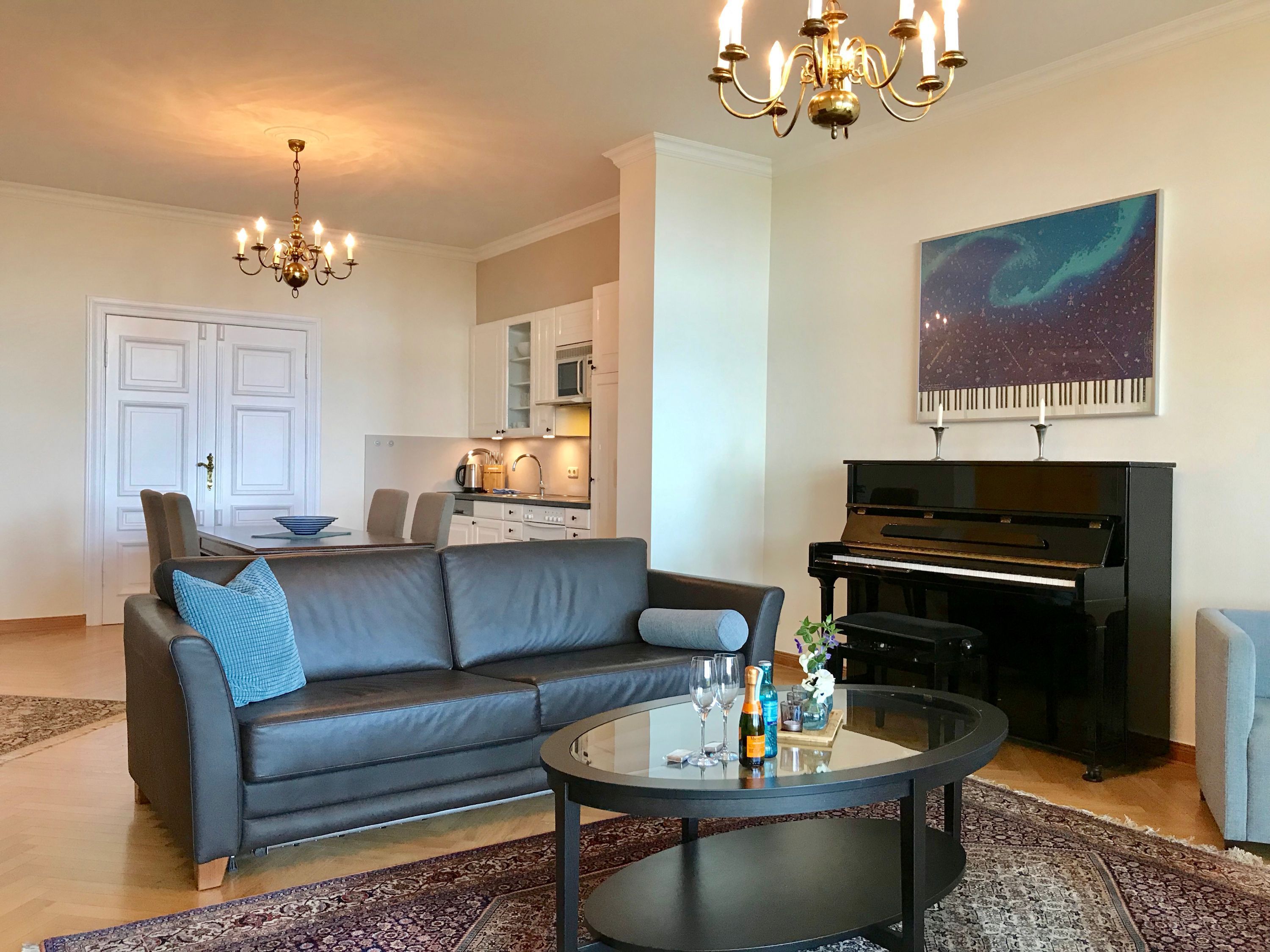 Una sala de estar con un sofá, una mesa de centro, una araña, un piano y un cuadro en la pared.