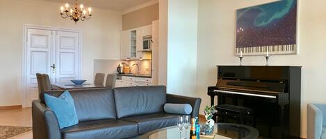 A living room with a sofa, coffee table, chandelier, piano, and a painting on the wall.