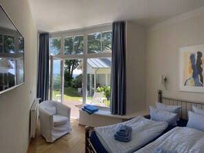 Ein Schlafzimmer mit großem Fenster, einem Bett, einem Sessel und Blick ins Freie.