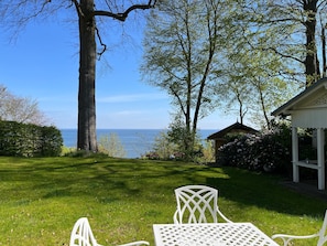 Un espace extérieur verdoyant avec une table et des chaises blanches, un kiosque et une vue sur la mer.