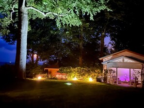 Ein Garten bei Nacht mit Laube, Bäumen und beleuchteten Wegen.