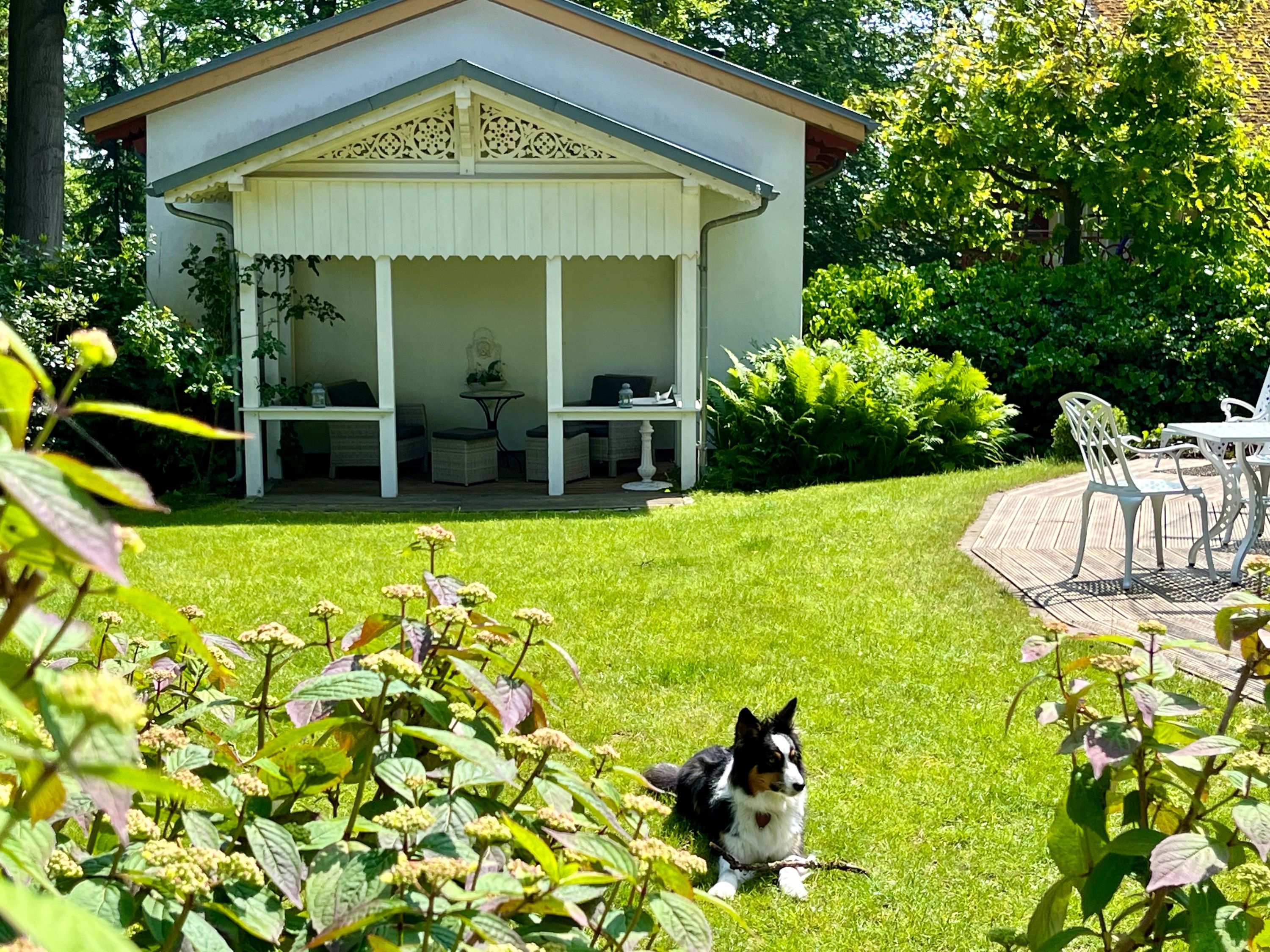A covered outdoor seating area with tables and chairs, surrounded by a well-maintained lawn and greenery.