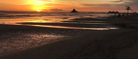 A beach with a sunset, a pier, and a lifeguard tower.