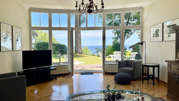 Un salon spacieux doté d’un grand téléviseur, de sièges confortables, d’une table en verre agrémentée d’objets décoratifs et offrant une vue sur la mer grâce à de grandes fenêtres.