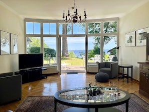 Un salon spacieux doté d’un grand téléviseur, de sièges confortables, d’une table en verre agrémentée d’objets décoratifs et offrant une vue sur la mer grâce à de grandes fenêtres.