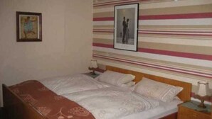 A bedroom with a bed, a nightstand, a lamp, and two framed pictures on the wall. - Room 5 - House by the forest (Lichtenfels)