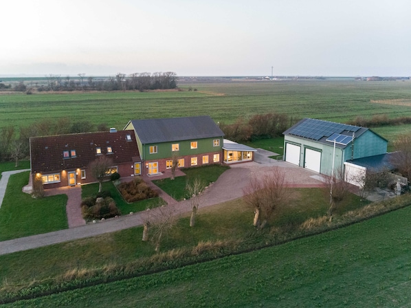 Une grande maison de plain-pied, à la façade verte et au toit gris, entourée d’une pelouse bien entretenue et d’un petit jardin.