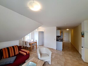 A compact living space with a dining area, kitchenette, and a cozy seating area with a sofa and armchair.