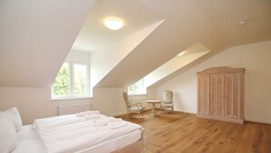 A bedroom with a large bed, a wooden wardrobe, a small round table, two chairs, and a window providing natural light. - Castle Apartment WE 29 - Hohendorf Castle (Groß Mohrdorf)