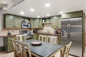 A kitchen with green cabinets, a stainless steel refrigerator, a microwave, and a dining table with chairs.