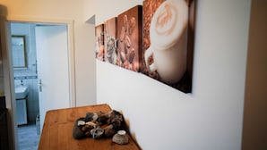 Un mur orné d’une série de tableaux sur le thème du café, une table en bois avec des pierres et une bougie, et une porte donnant sur une salle de bain.