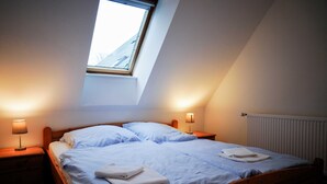 Une chambre avec un plafond en pente, un puits de lumière, un lit avec du linge de lit blanc, deux lampes de chevet et un radiateur.