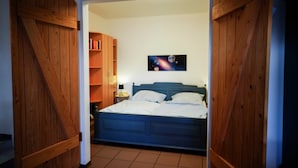 A bedroom with a blue bed, wooden walls, a bookshelf, and a space-themed painting.
