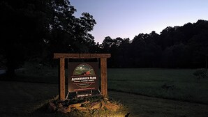 Segnale per l'Agriturismo Altenbrauch con il logo di un evento di campeggio, circondato da erba e alberi.