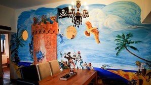 Ein Essbereich mit einer Wandmalerei von Piraten und einer Burg, einer Kristallleuchtre und einem Holztisch mit Stühlen.