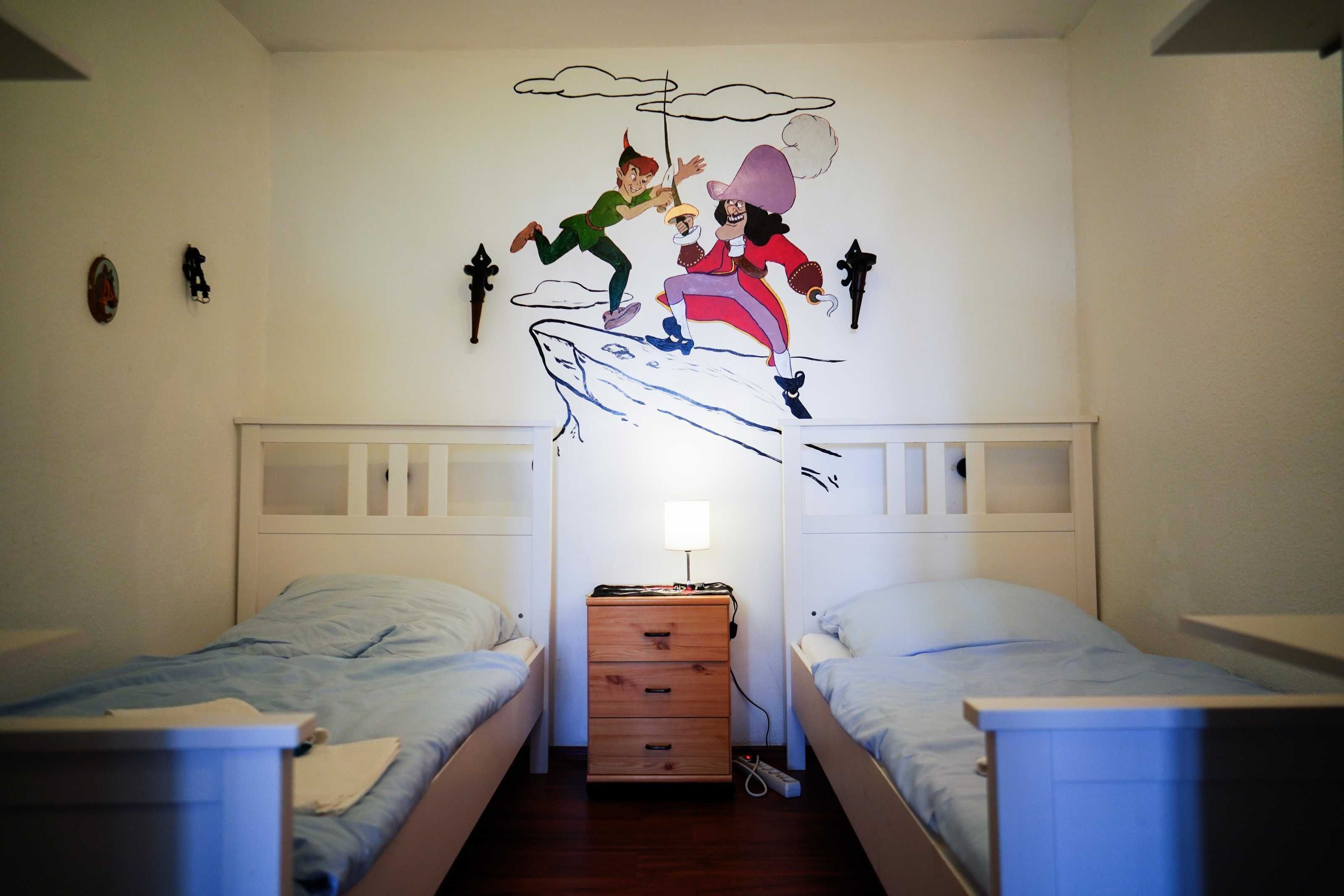Habitación con dos camas individuales, un aparador de madera y un mural en la pared que muestra a dos personajes en una tabla de surf.
