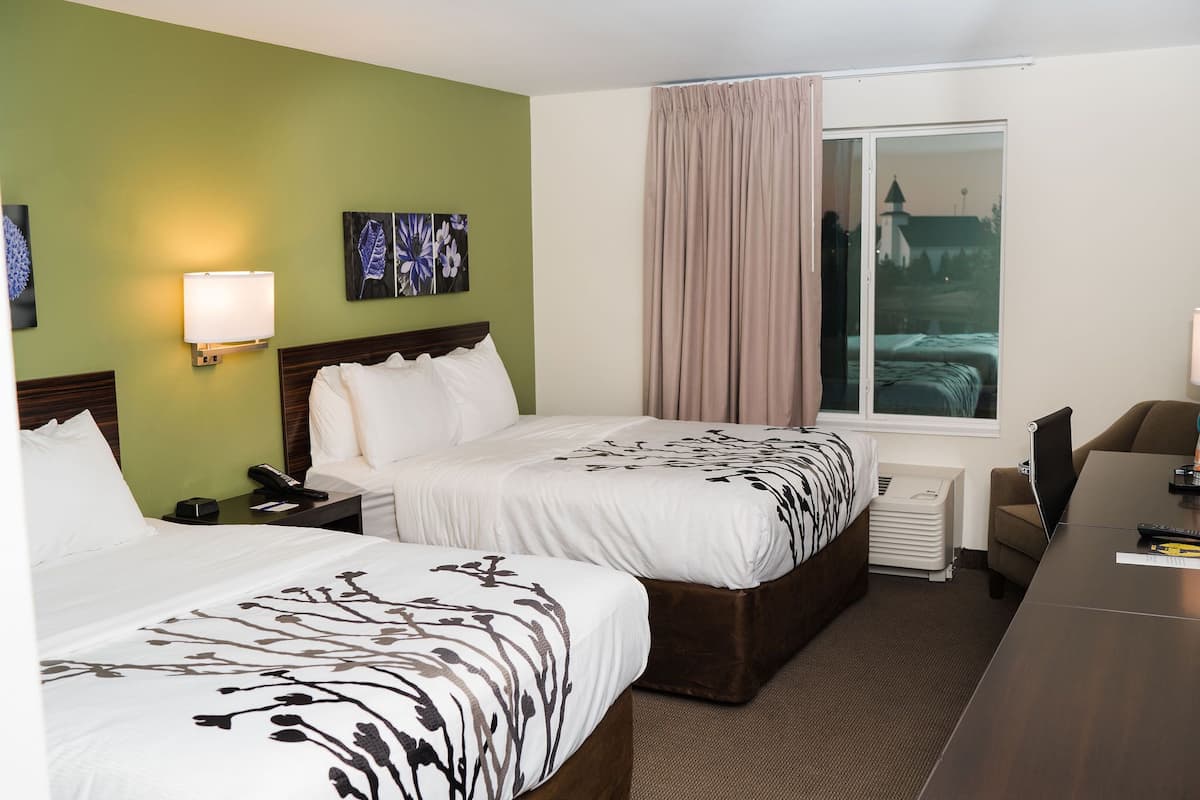 A hotel room with two beds, a desk, a chair, a lamp, a phone, and a window with curtains.