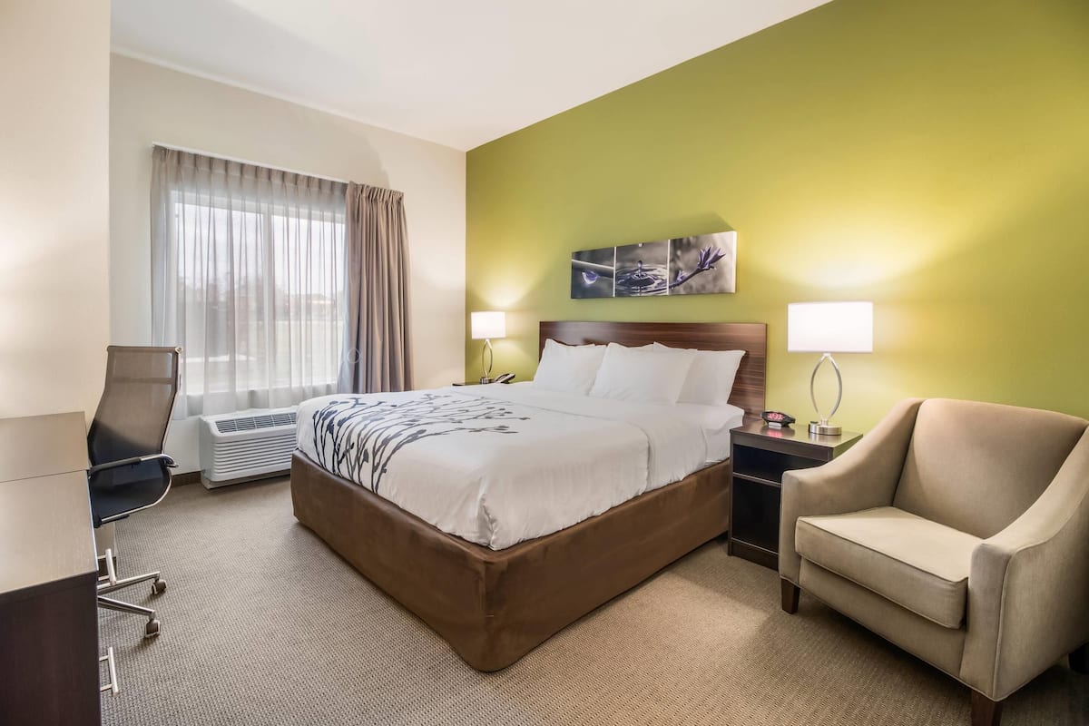 A hotel room with a large bed, a desk, a chair, and a window with curtains.