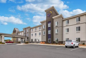 A Sleep Inn hotel with a modern design, featuring a covered entrance, multiple floors, and a parking lot with vehicles.