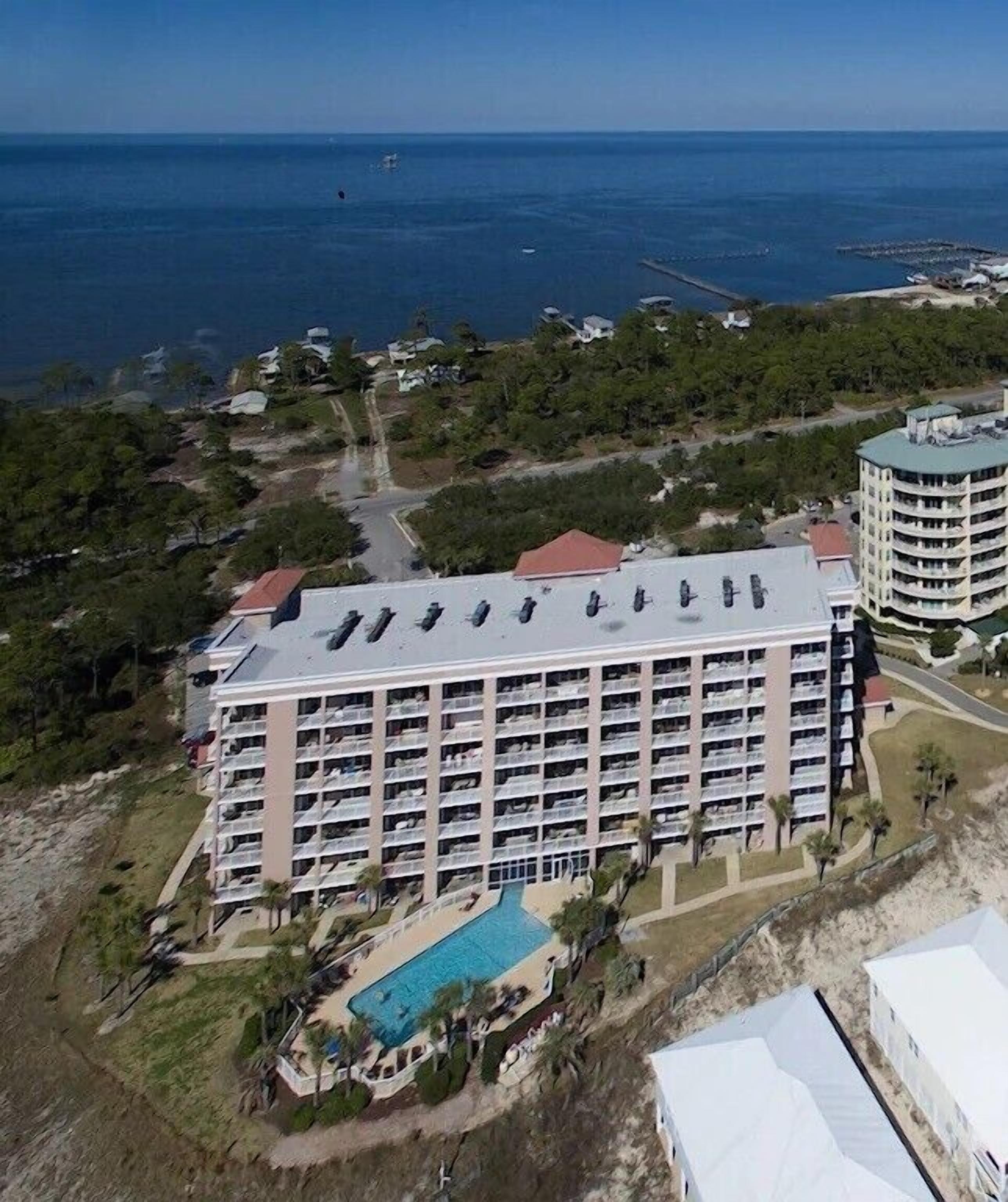 A large hotel with multiple floors, a swimming pool, and a view of the ocean.