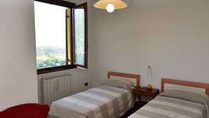 Une chambre avec deux lits, un fauteuil rouge, une fenêtre donnant sur un beau paysage et une lampe suspendue.