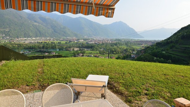 Une terrasse avec des sièges extérieurs, offrant une vue sur une vallée, des montagnes et une ville au loin.