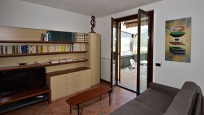 Un salon comprenant une bibliothèque, un téléviseur, un banc, un canapé et une porte-fenêtre coulissante donnant sur un espace extérieur.