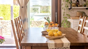 Een houten eettafel met een witte kant tafelkleed, een schaal met citroenen en glazen jus d'orange.