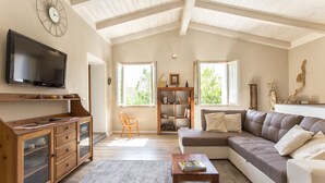 Een ruime woonkamer met een houten kast, een grote flatscreen-tv, een bank en een salontafel.