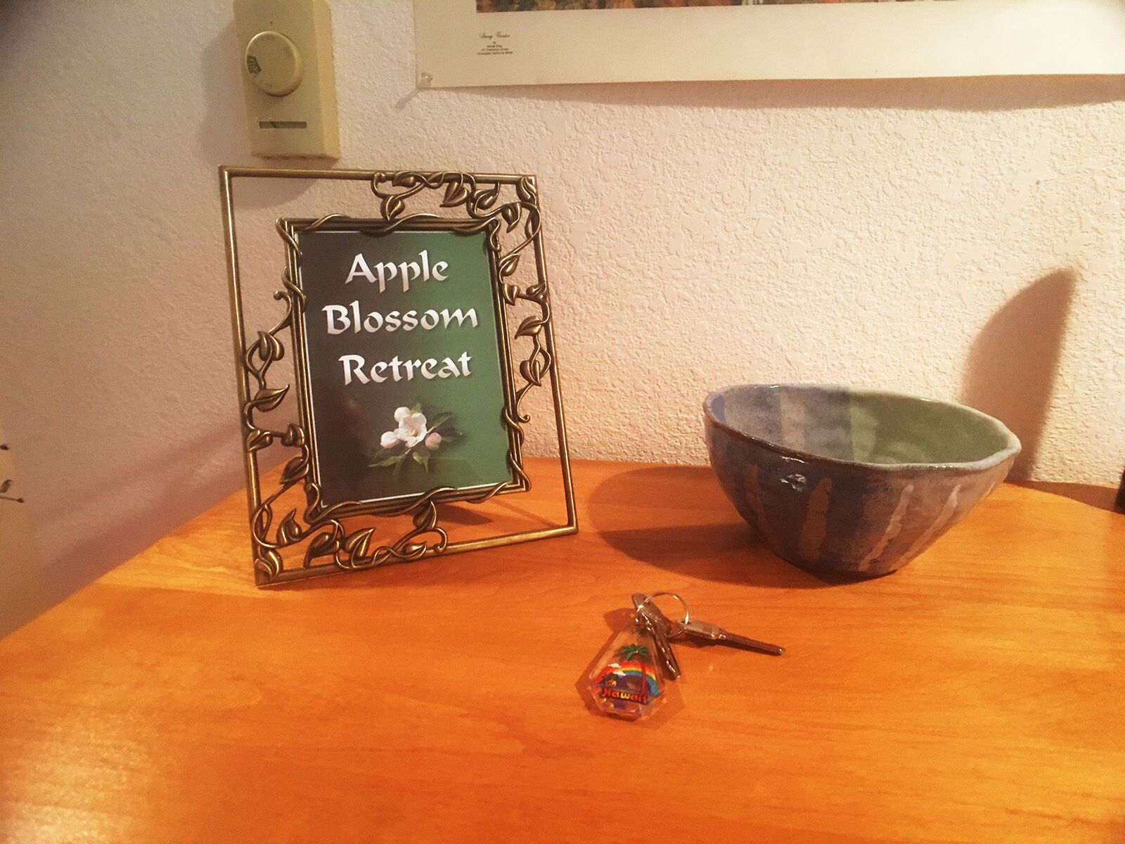 A framed sign with "Apple Blossom Retreat" text, a bowl, and a keychain on a wooden table.