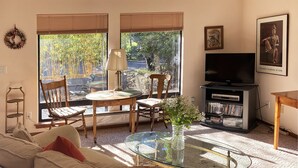 Una sala de estar con sofá, mesa de centro de vidrio, televisor, estantería y ventana con persianas.